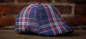 The Brave cap is here featuring a blue, red and white plaid. Cap shown against a brick wall.